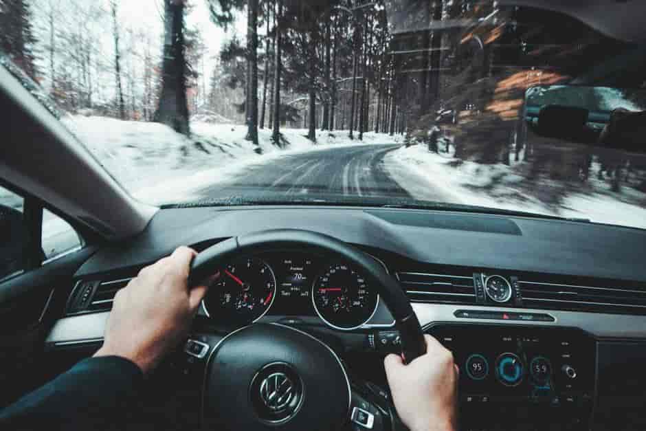 Driver’s perspective of a Volkswagen steering wheel and dashboard as the car travels along a snow-covered forest road
