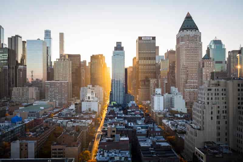 Aerial view of a city skyline at sunset with golden sunlight streaming between glass skyscrapers.